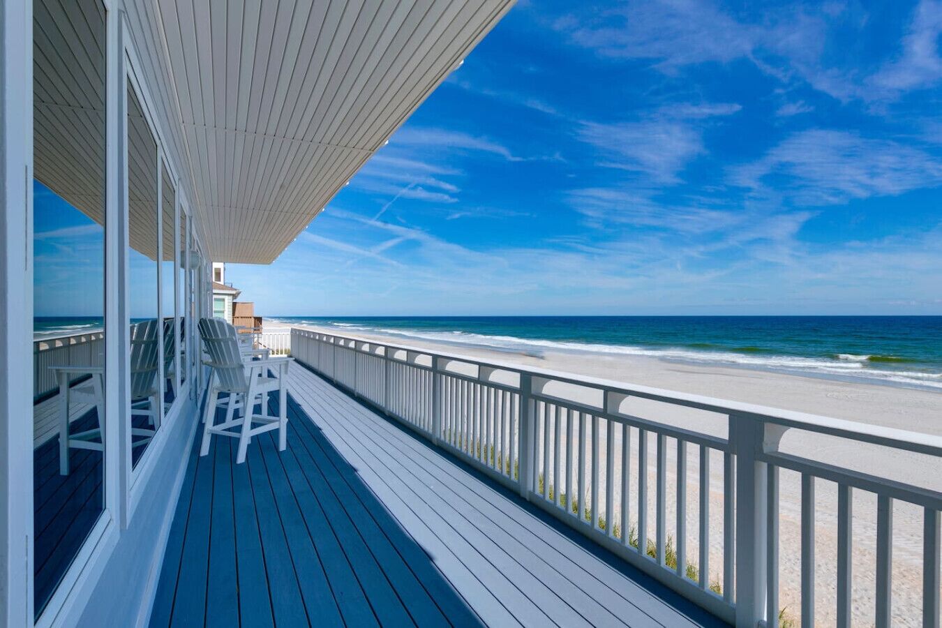 Una terraza de madera con barandillas blancas que da a una playa.
