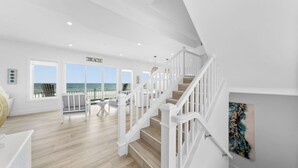 Un intérieur spacieux avec un escalier menant à un balcon d’où l’on a vue sur la plage.