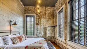 A bedroom with a bed, bench, and large windows with blinds.