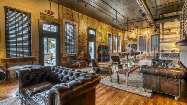 A spacious room with a large leather sofa, wooden flooring, and a rustic brick wall.