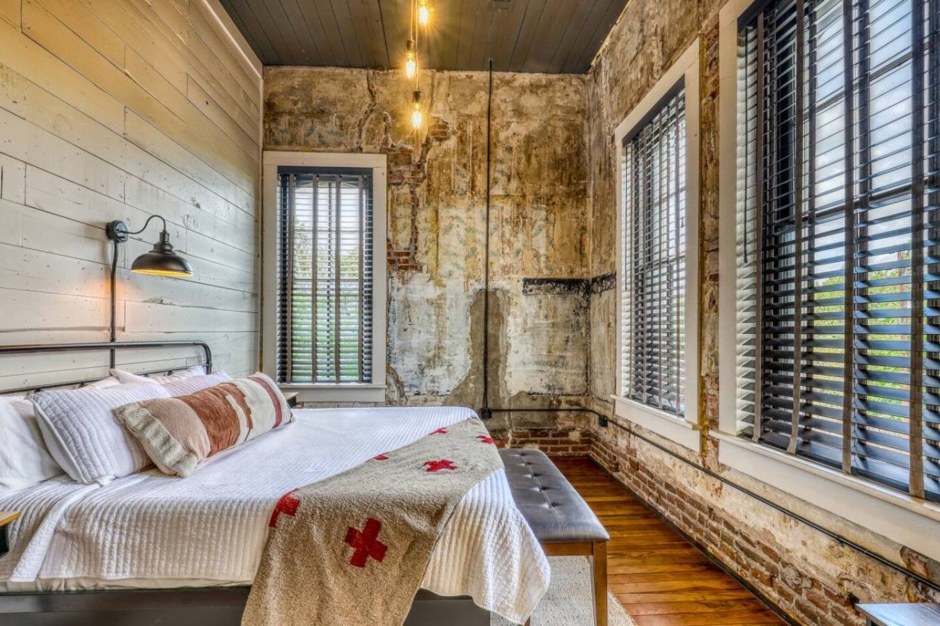A bedroom with a bed, a bench, and a window with blinds.