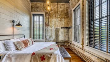 A bedroom with a bed, a bench, and a window with blinds.