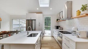 A modern kitchen with white cabinetry, a central island with a sink, stainless steel appliances, and a skylight. - Modern Rustic Private Ranch w/ Peloton! (Henryville)