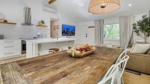 A modern kitchen with white cabinetry, a wooden dining table, and a hanging light fixture. - Modern Rustic Private Ranch w/ Peloton! (Henryville)