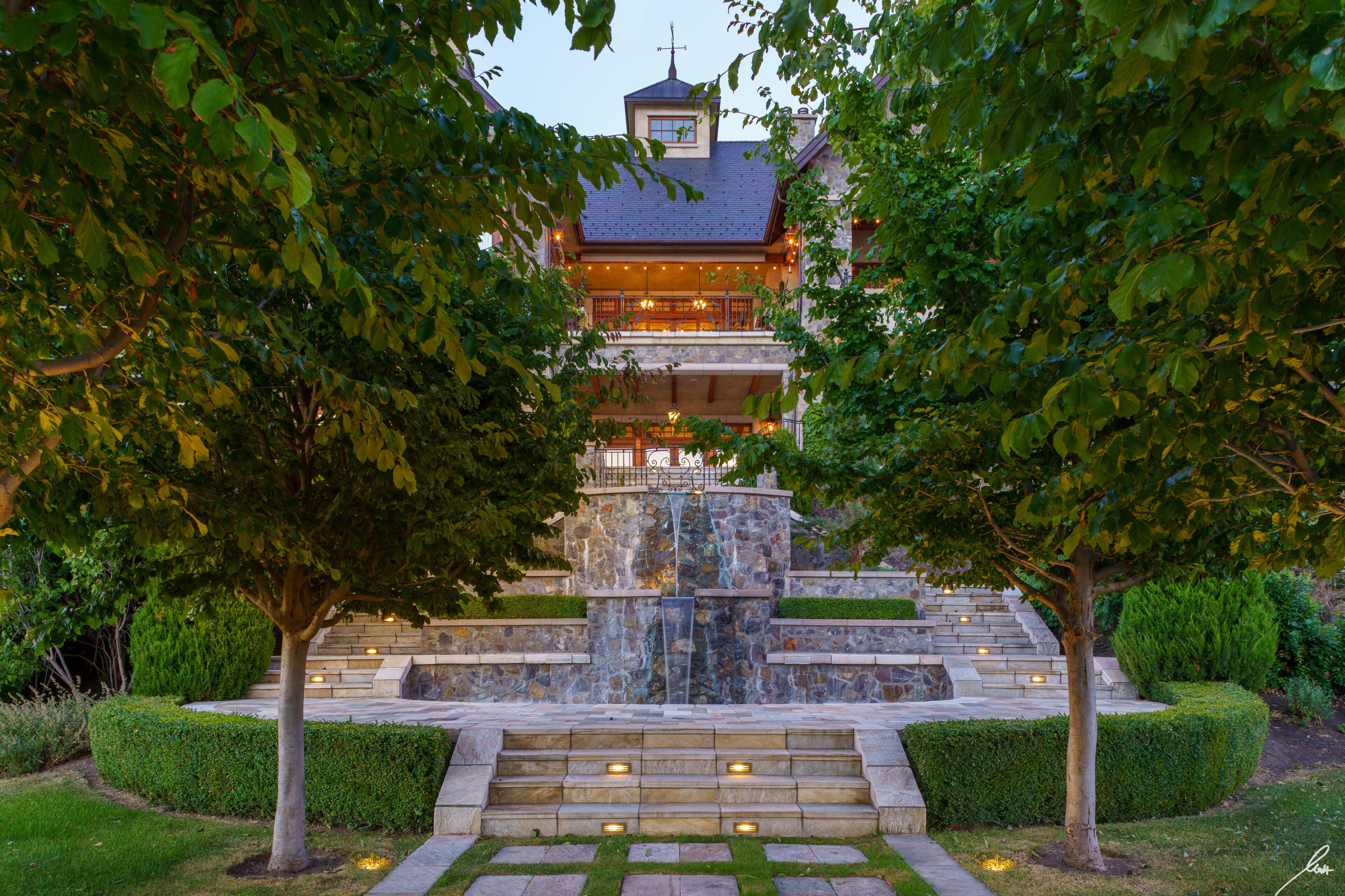 A stone staircase leading to a building with a balcony and a waterfall feature.
