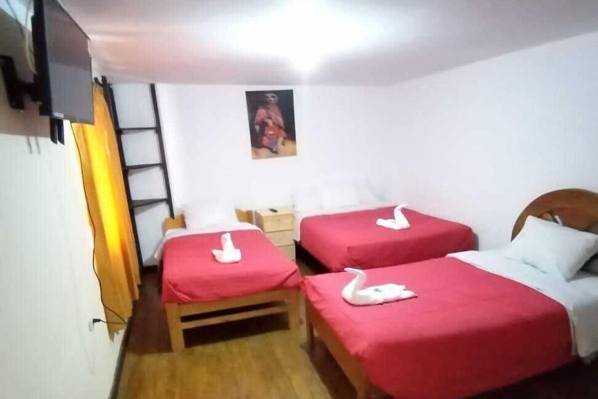 A small, cozy room with two single beds, a wooden floor, a wall-mounted TV, and a small table with a lamp.