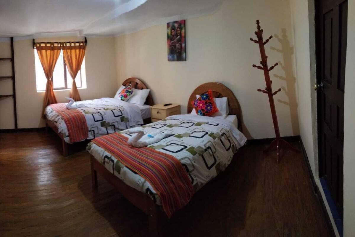 A bedroom with two beds, wooden flooring, a ladder, and a door.