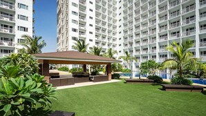 Een hotel binnenplaats met een overdekt zitgedeelte, kunstgras en palmstruiken.