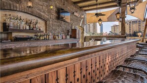 A bar area with a stone wall, wooden bar counter, and hanging lights.