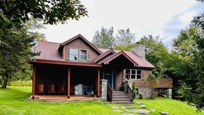 Une cabane en rondins dotée d’un porche couvert, d’un escalier en pierre et d’une cheminée en pierre.