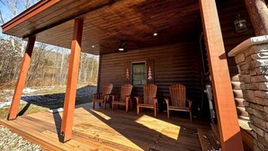 Une cabane en bois dotée d’un porche couvert, de meubles d’extérieur et d’une cheminée en pierre.