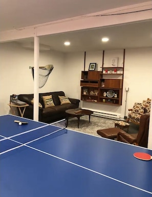 A living room with a ping pong table, a sofa, a coffee table, and a bookshelf.