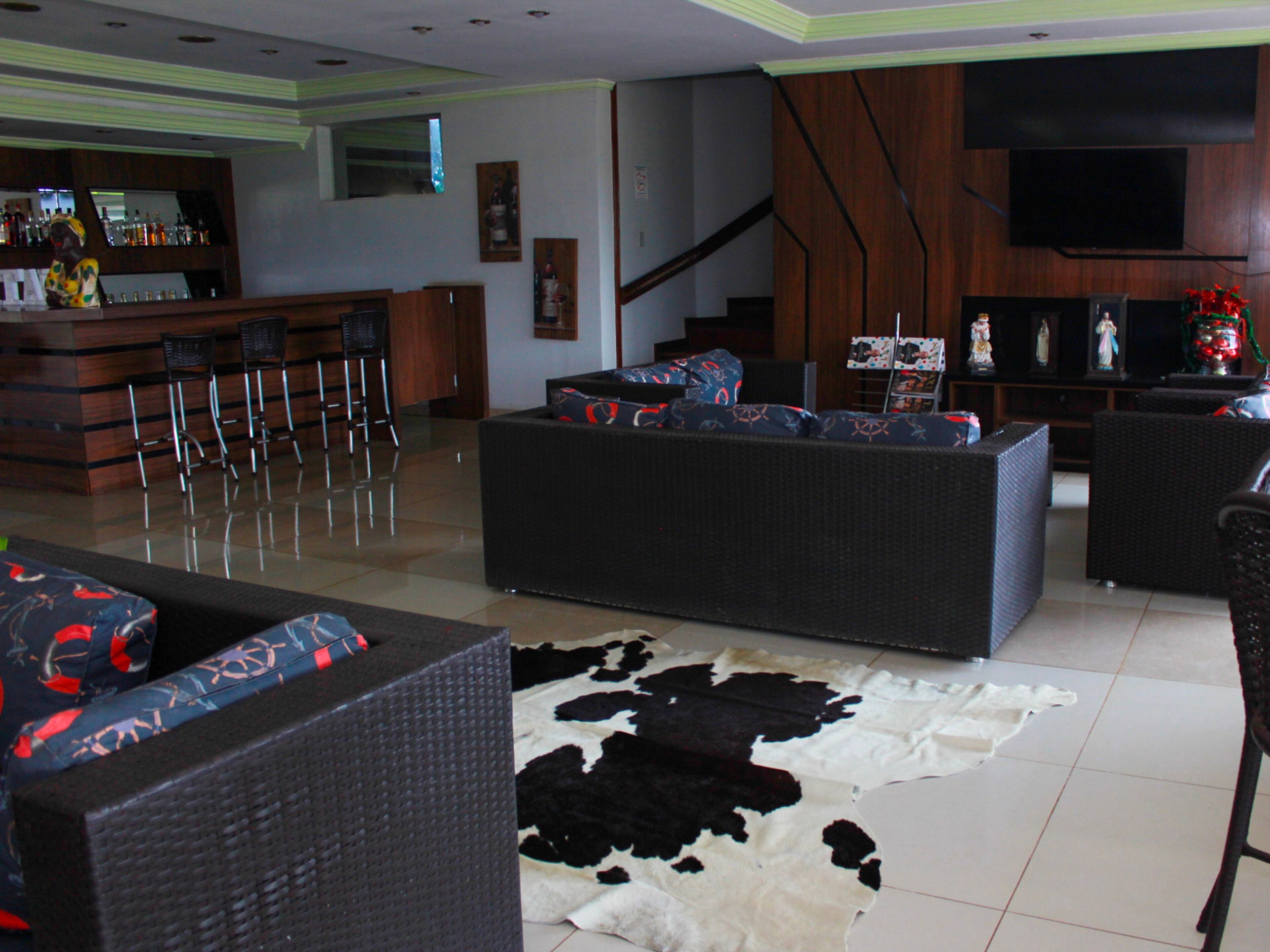 Una sala de estar con sofá, alfombra de cuero, zona de bar con taburetes y una escalera.