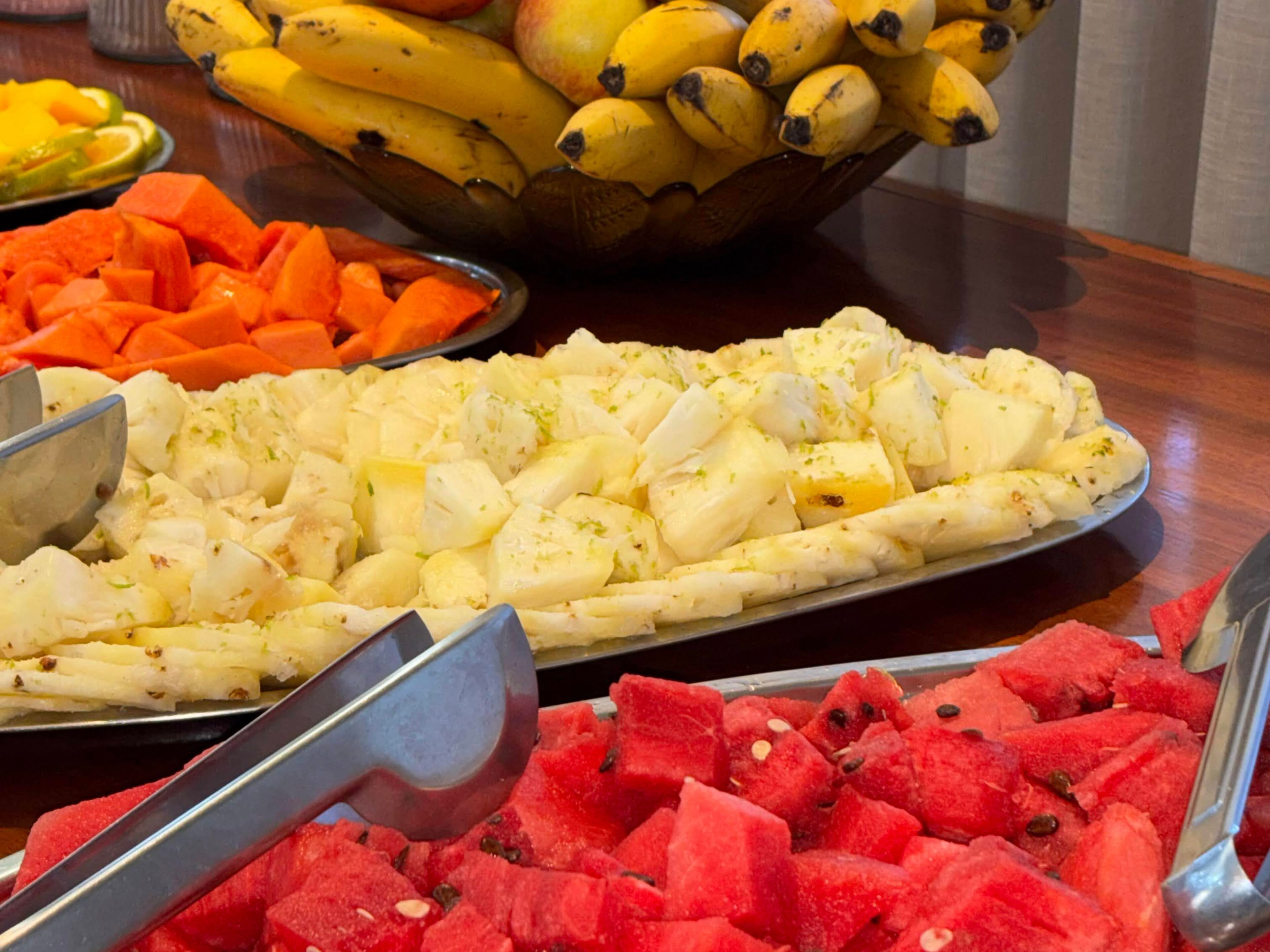 A buffet with various fruits and vegetables, including bananas, carrots, and watermelon.