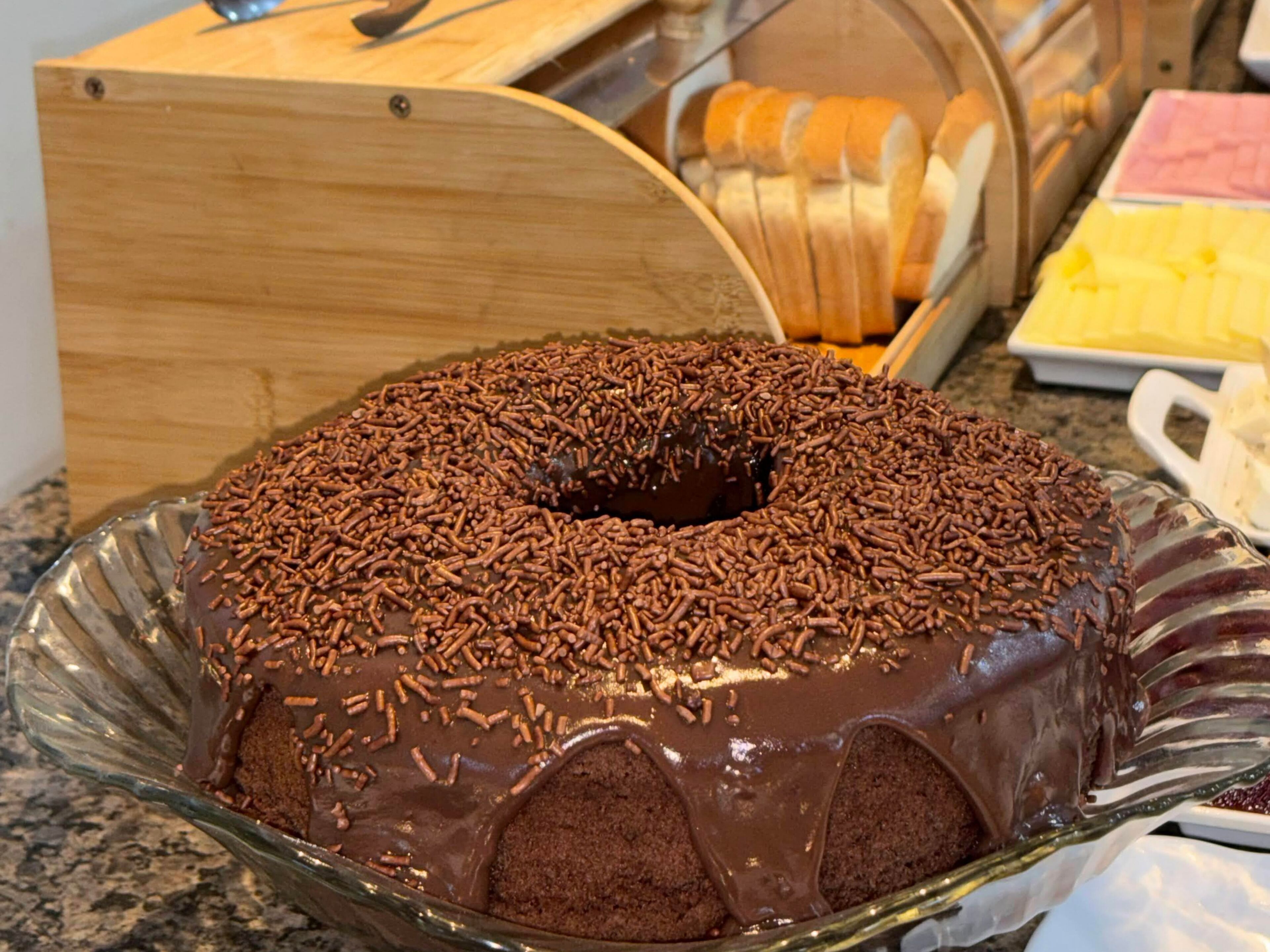 A chocolate bundt cake with chocolate sprinkles on a glass plate.