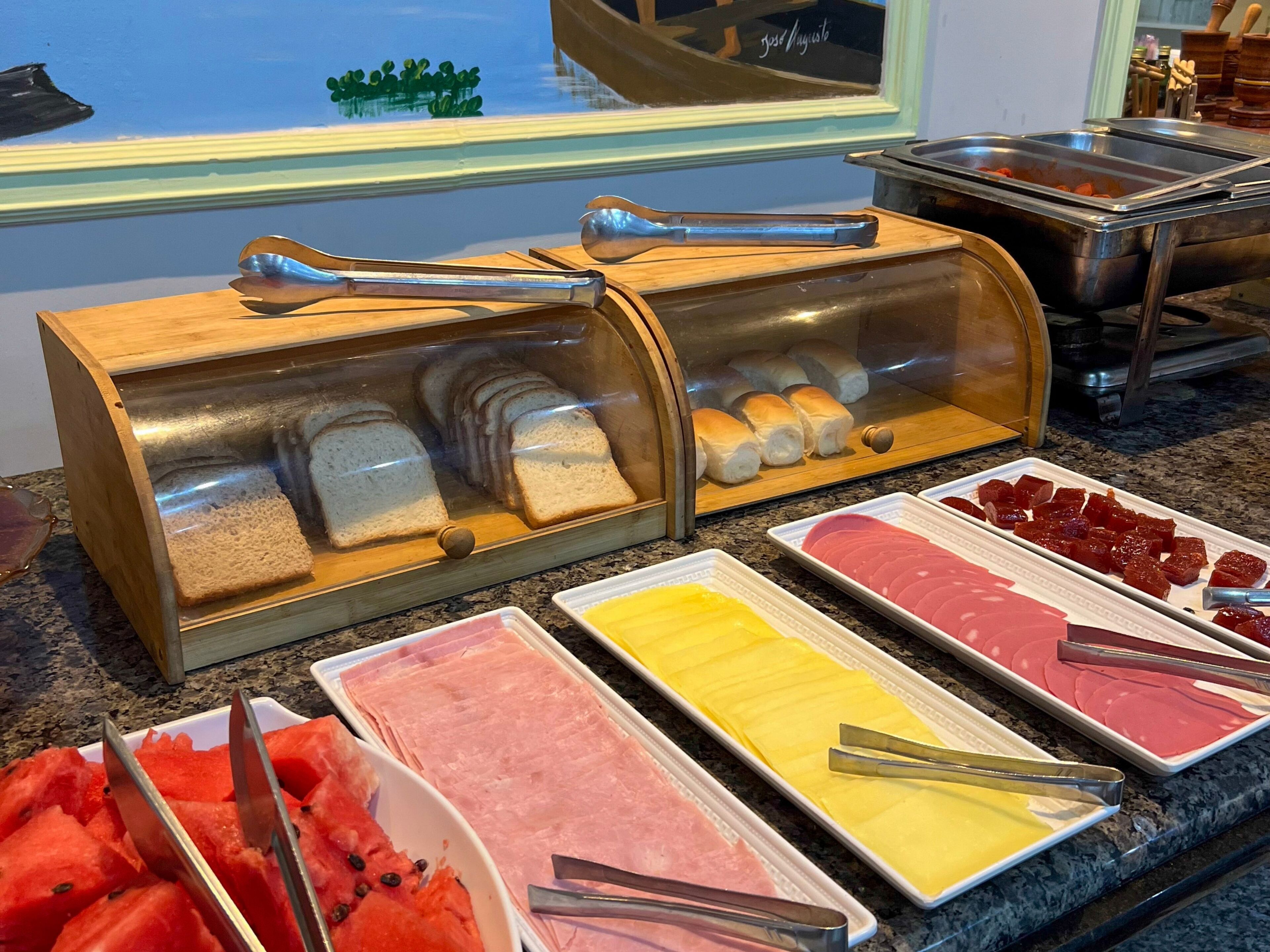 Un bufé con diversos alimentos, como pan, jamón y sandía.