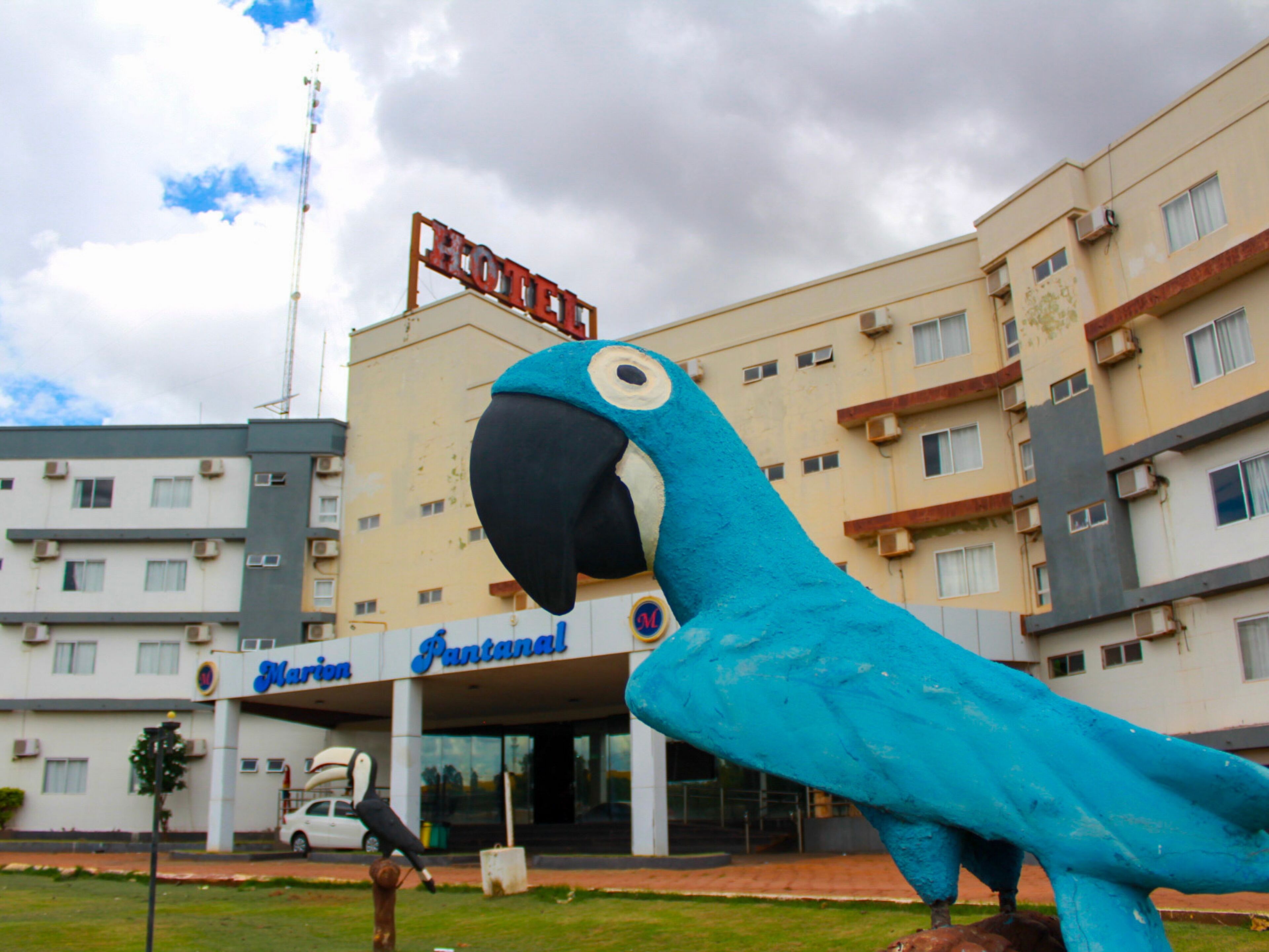 Una gran escultura de un loro azul frente a un hotel con varios pisos y balcones.