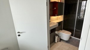 A compact bathroom with a toilet, a small shelf with a potted plant, a towel rack, and a shower area. - Charming 2-bed Apartment in London (London)