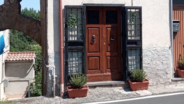 Un edificio con fachada rústica, un doble puerta de madera y dos macetas en la entrada.