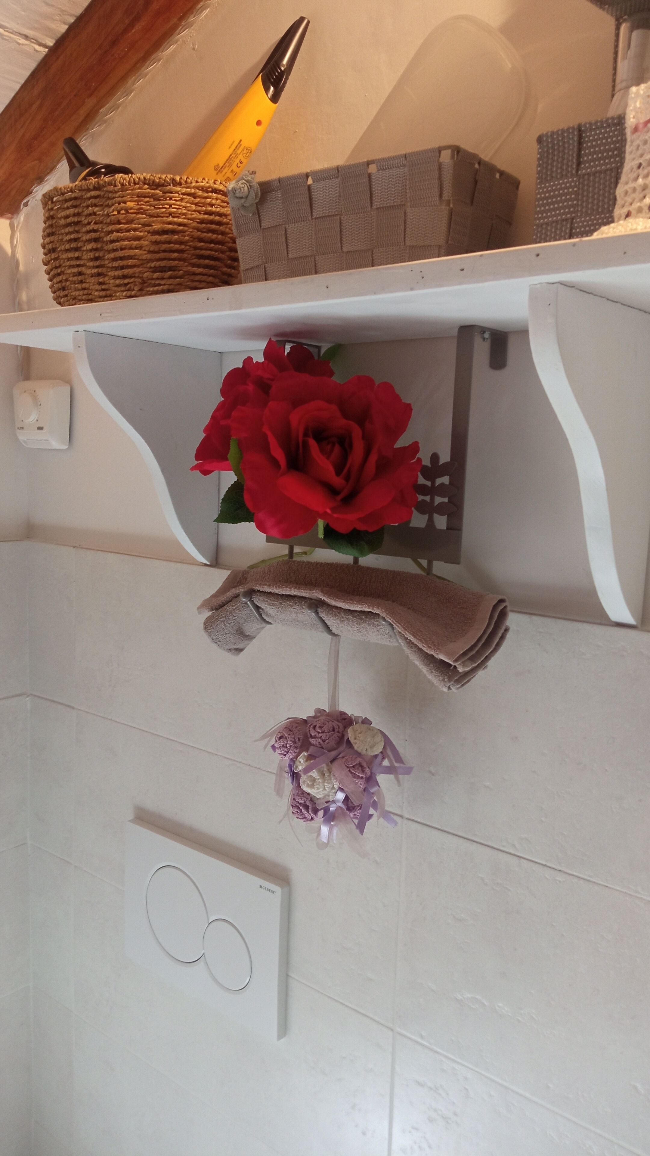 Un baño con una bañera blanca, un perchero con una rosa roja y una toalla decorativa.