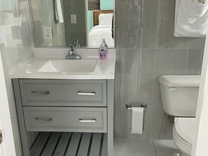 A bathroom with a white sink, two drawers, a mirror, a toilet, and a towel hanging on the wall.