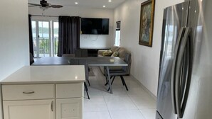 Una cocina moderna con un refrigerador grande, un comedor con mesa y sillas, un televisor de pantalla plana en la pared y un ventilador de techo.