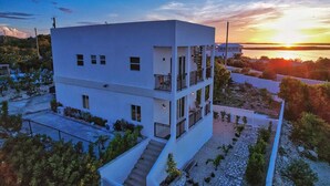 Un edificio moderno de varios pisos con techo plano, un balcón en el nivel superior y una escalera que conduce a la entrada.