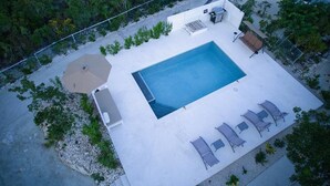 Vista aérea de una piscina rectangular con solárium blanco, rodeada de sillas de descanso y una mesa.