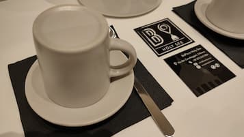 A coffee cup on a saucer with a napkin and a spoon beside it, and a business card with contact information.