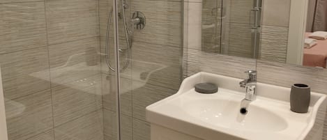 Une salle de bain moderne avec une douche à parois de verre, un lavabo blanc agrémenté d’un vase et un miroir.