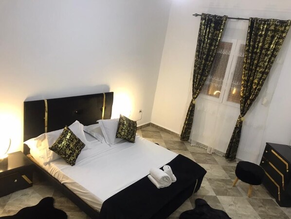 A neatly made bed with white linens and two patterned pillows, a bedside table with a lamp, and a black nightstand.