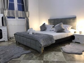 A bedroom with a bed, nightstands, a dresser, and a window with curtains.