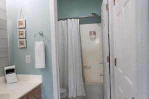 Une salle de bain avec une douche, des toilettes et un lavabo. On y trouve un porte-serviettes avec une serviette et un coussin sur lequel est écrit le mot « maquillage ».