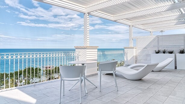 Un espacio de esparcimiento al aire libre moderno con sillas blancas y una mesa, con vistas a la costa.