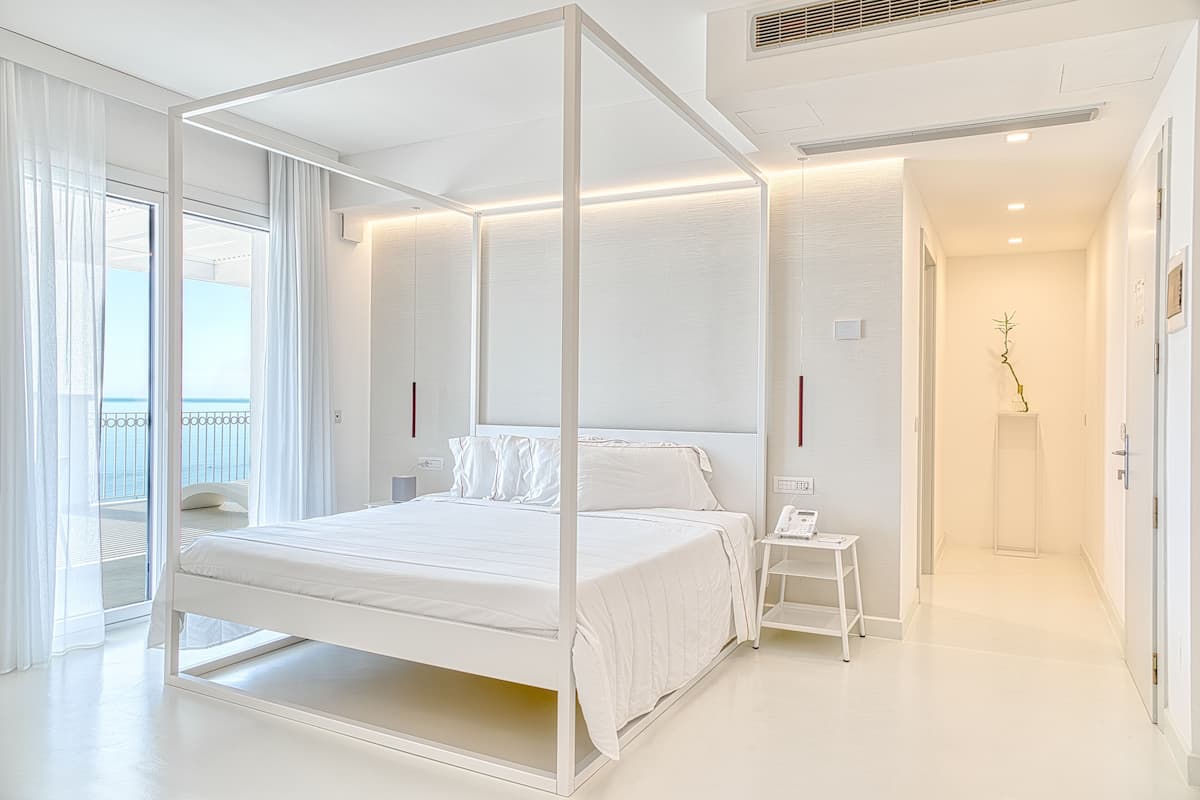 Moderni hotellihuone, jossa on suuri sänky, pieni yöpöytä ja näkymä parvekkeelle.