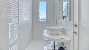Un baño moderno con un lavamanos blanco, un perchero para toallas y una ventana que ofrece vistas al cielo.