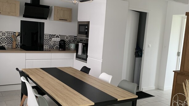 A modern kitchen with a central island, white cabinetry, and a black and wood dining table with six chairs.