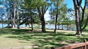 Un parque con un banco de madera, árboles y un lago al fondo.