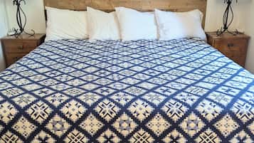 Una cama con una colcha estampada, cabecera de madera, dos mesitas de noche con lámparas y suelo de madera.