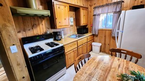 A wooden-paneled kitchen with a stove, microwave, sink, and refrigerator.