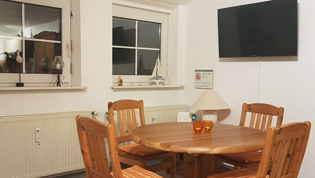 Un comedor con mesa y sillas de madera, una ventana con vistas y un televisor de pantalla plana montado.
