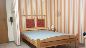 Una cama individual con estructura de madera y colchón azul en una habitación con papel tapiz a rayas y piso de madera.