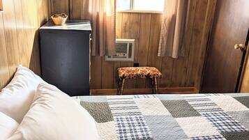 Un dormitorio con una cama, una mesita de noche, una lámpara, una ventana con cortinas y una puerta.