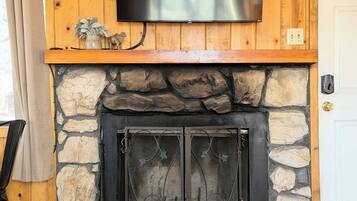 Una chimenea de piedra con un televisor de pantalla plana encima, un fuste de madera y una puerta a la derecha.