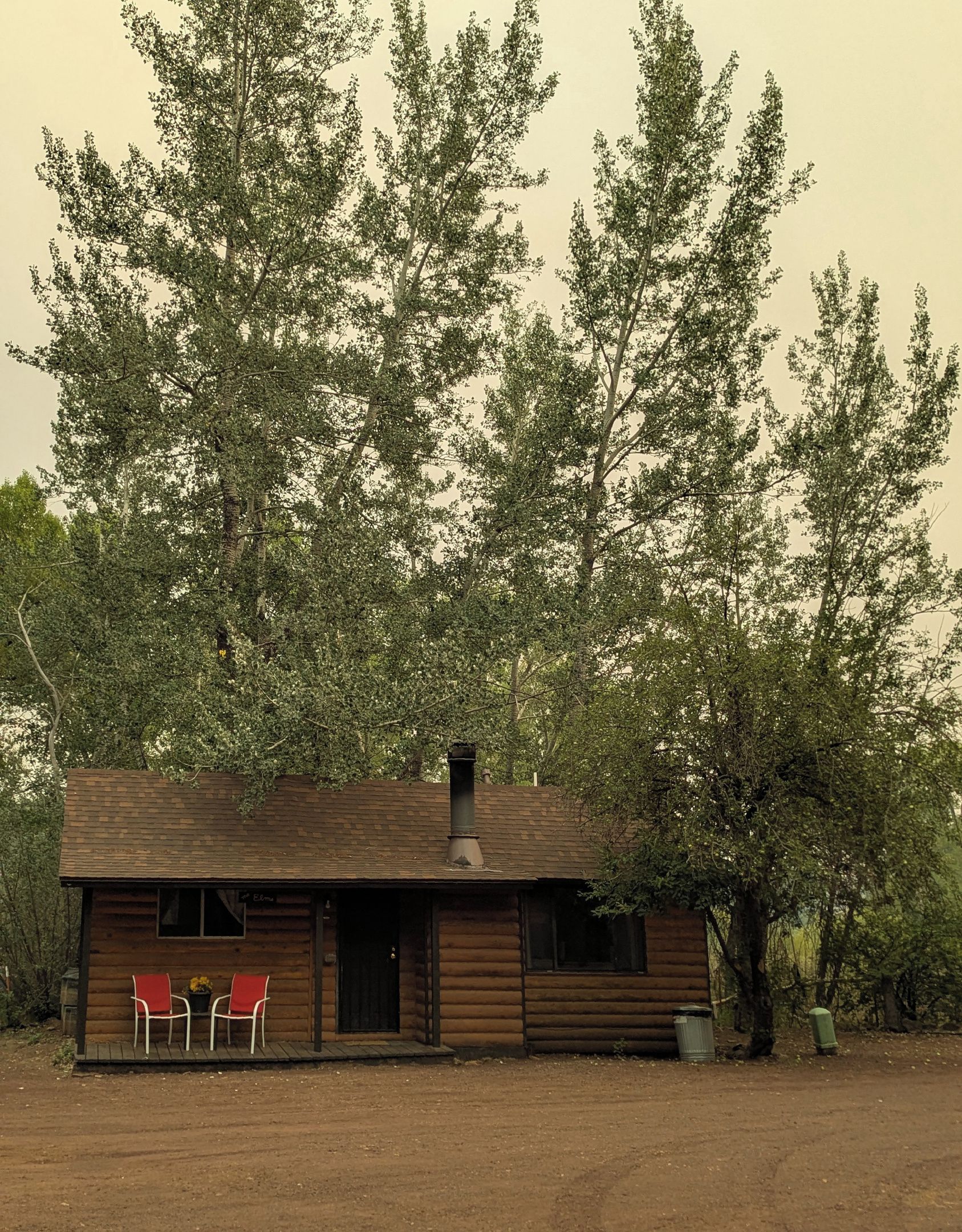 A rustic cabin with a chimney, two red chairs, and a small table.