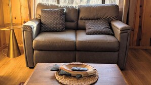 A cozy room with a leather sofa, a woven coffee table, and a lamp. - Elms Cabin at Lazy Oaks Resort (Lakeside)