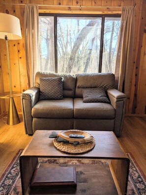 A cozy room with a leather sofa, a woven coffee table, and a lamp. - Elms Cabin at Lazy Oaks Resort (Lakeside)