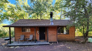 Una cabaña de troncos con chimenea, dos sillas y una pequeña terraza.