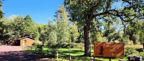 A sign for Oaks Resort with a wooden fence and a dirt path leading to a cabin.