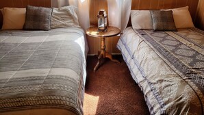 Une chambre avec deux lits, une petite table sur laquelle se trouve une lanterne, et une fenêtre avec des rideaux.